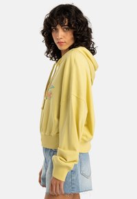 Yellow hooded sweatshirt with a relaxed fit, drawstrings, and a graphic design. Soft fabric and ribbed cuffs complete the look.
