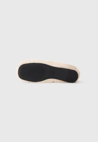 Flat sole of a slipper, featuring a black rubber base with ribbed texture and a light beige, plush material along the edges.