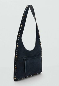 Granatowa zamszowa torba na ramię ozdobiona ćwiekami w kolorze złotym i srebrnym, o zaokrąglonym kształcie oraz z przednią kieszenią zapinaną na zamek.