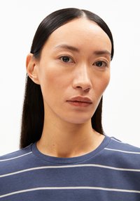 Blauw gestreept shirt met witte horizontale strepen, ronde halslijn, zachte stof, het gezicht van het model gedeeltelijk zichtbaar, steil zwart haar.