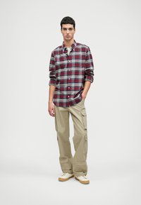 Piros és tengerészkék kockás, gombos ing hosszú ujjal, bézs cargo nadrággal, amely több zsebbel és szűkített fazonnal rendelkezik. Fehér sportcipők.