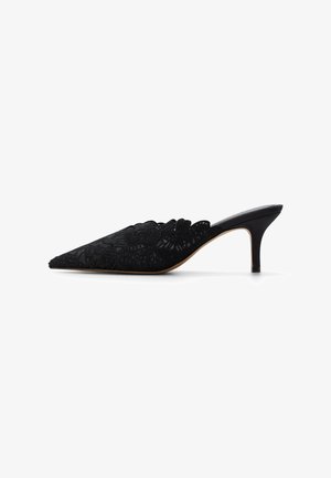 Mules noires pointues avec superposition de dentelle, bord festonné et talon fin effilé. Doublure intérieure lisse et design stiletto.