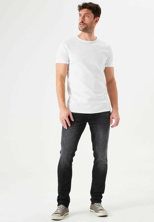 Camiseta blanca de manga corta combinada con jeans de lavado oscuro y zapatillas grises. El conjunto presenta un ajuste clásico y un diseño sencillo.