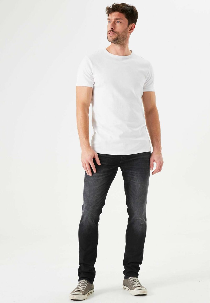 Camiseta blanca de manga corta combinada con jeans de lavado oscuro y zapatillas grises. El conjunto presenta un ajuste clásico y un diseño sencillo.