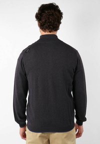 Pull en maille gris foncé avec un col haut, texture tricotée et poignets côtelés, présentant une petite étiquette de marque sur l'épaule gauche.