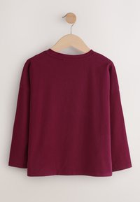 Bordeauxrotes Langarmshirt aus Baumwolle. Verfügt über einen Rundhalsausschnitt und überschnittene Schultern. Glatte Textur mit geradem Saum und ohne sichtbare Verschlüsse.