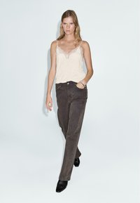 Top en satin beige avec dentelle, associé à un jean droit marron foncé. Des bottines noires à talons complètent la tenue.