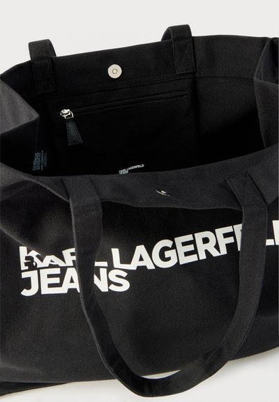 Черен чанта тип тоте с бял надпис "KARL LAGERFELD JEANS", две дръжки, магнитно закопчаване и видим вътрешен джоб с цип.