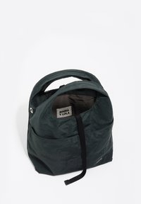 Plecak z ciemnozielonego materiału o fakturowanym wykończeniu, z górnym uchwytem i przednią kieszenią. Wnętrze zawiera oznaczoną metkę. Prostota i funkcjonalny design.