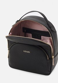 Zaino nero con texture e zip dorate. L'interno è foderato in rosa e presenta una tasca con zip, etichettata con il nome del marchio "LIU-JO."