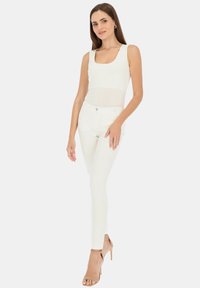 Biały dopasowany top na ramiączkach z kwadratowym dekoltem w połączeniu z białymi obcisłymi dżinsami; modelka nosi beżowe sandały na obcasie. Prosty, czysty design.