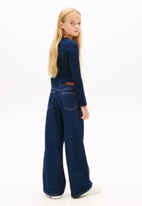 Mornarsko modra dolg rokav s rebrastim vzorcem, kombiniran z visokim pasom širokih kavbojk iz jeansa. Kavbojke imajo rjav usnjen žepni dodatek in klasične žepe.