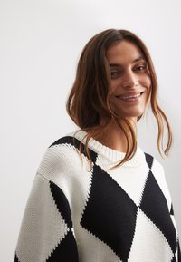 Strickpullover in Weiß und Schwarz mit einem Diamantmuster. Verfügt über einen Rundhalsausschnitt und lange Ärmel mit einer strukturierten Oberfläche.