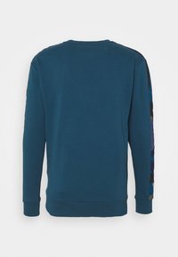 Teal crewneck sweatshirt med långa ärmar; har ett mönstrat tyg längs ärmarna och en ribbad nederkant och ärmslut. Slät textur.