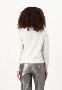 Pull en tricot blanc à la coupe ajustée et aux poignets côtelés, associé à un pantalon argenté métallique avec un détail de logo triangulaire.