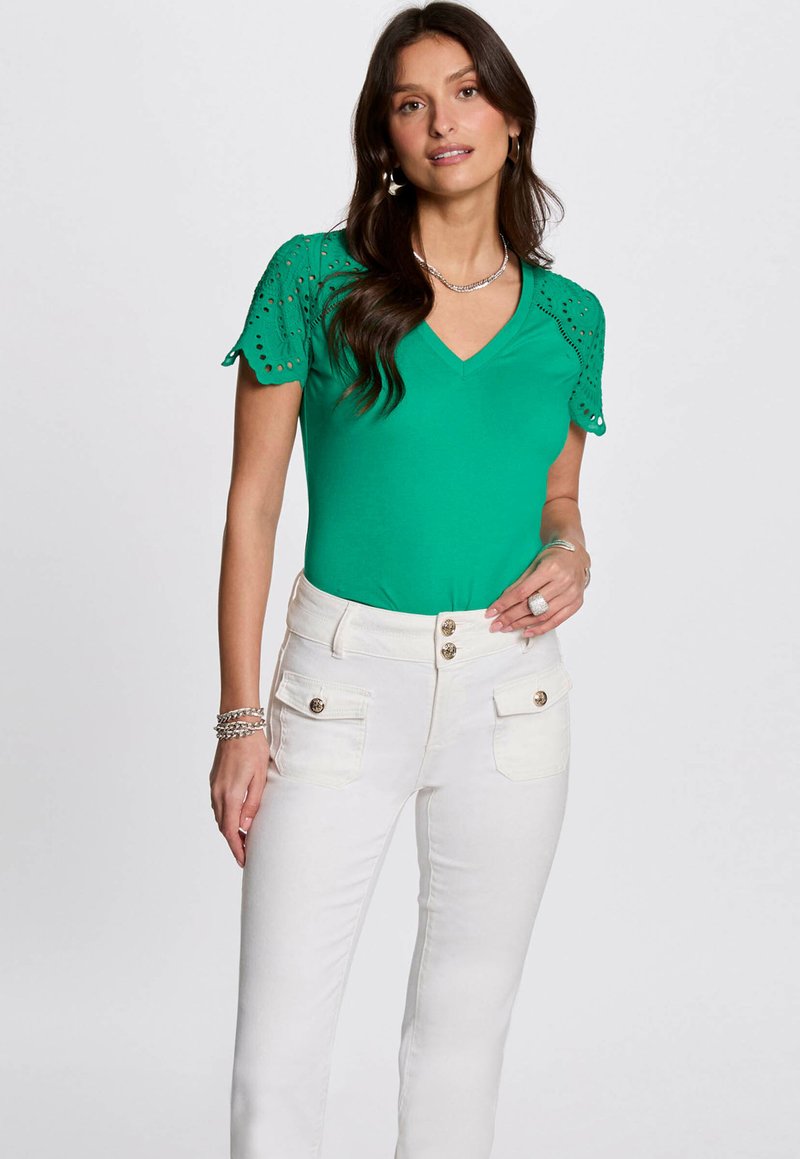 Top verde de manga corta con detalles de encaje en las mangas, escote en V; combinado con pantalones blancos de talle alto con bolsillos frontales y botones.