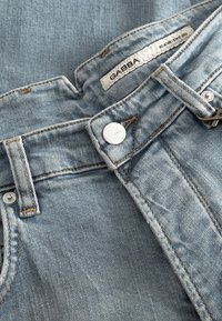 Lichtblauwe denim jeans met een hoge taille, voorzien van zilverkleurige hardware, oranje stiksel en een merklabel aan de binnenkant van de tailleband.