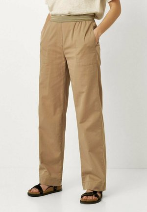 Beige wide-leg pants with an elastic waistband, featuring side pockets and a smooth cotton texture, paired with strappy black sandals.