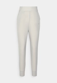 Jasnoszare spodnie sportowe wykonane z gładkiego, elastycznego materiału, o dopasowanym kroju, zwężanych mankietach oraz małym logo Nike po lewej stronie.