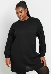 Abito maglione nero a costine con maniche lunghe e scollatura rotonda. La trama è morbida e la vestibilità sembra rilassata e oversize.