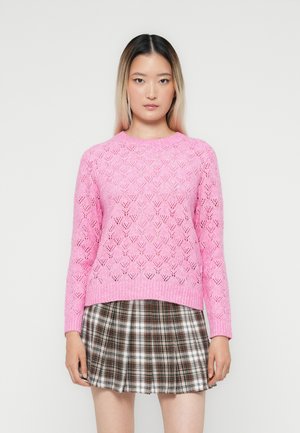 Pulover roz din tricot, cu model de diamant decupat, guler rotund și manșete cu nervuri, combinat cu o fustă în carouri în nuanțe de maron și alb.