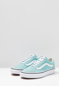 Baskets en daim bleu clair avec des bandes blanches accentuées, une semelle blanche et des lacets plats blancs. Fini texturé avec une garniture noire contrastante.