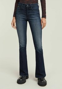 Dark blue flared jeans made from denim. Features a high waist, subtle fading, and side pockets. Paired with black platform shoes.