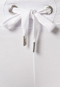 Vita byxor med elastisk midja, med dragsko i vit tyg, metallöglor och silverdetaljer.