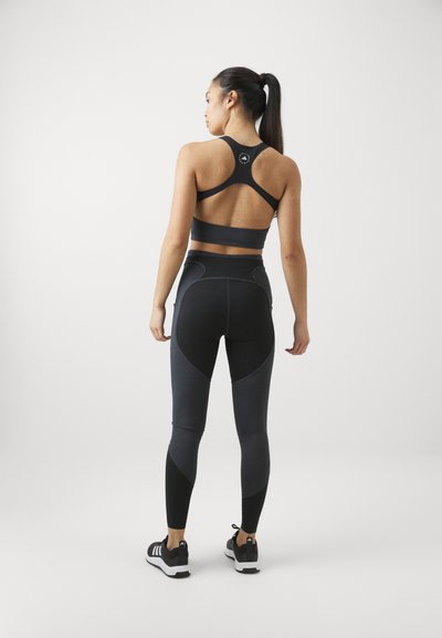 Svart sporty bh med racerback-design, kombinert med høy midje tights med kontrasterende mørke paneler. Materialet ser ut til å være elastisk og teksturert.