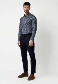 Langärmliges, knöpfbares Hemd in Marineblau mit floralem Muster, kombiniert mit dunklen Hosen und braunen Wildlederschuhen. Glatte Stoffqualität, taillierte Passform.