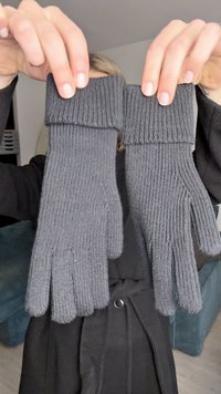 Szürke kötött kesztyű, bordás mandzsettával, texturált anyagból és külön ujjnyílásokkal, egy semleges háttér előtt van tartva.