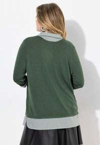 Maglia verde a maniche lunghe con collare a righe e orlo. Presenta una vestibilità comoda e una texture morbida, abbinata a una gonna di pelle nera.