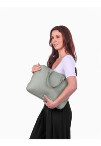 Grüne Kunstleder-Handtasche mit runden Griffen, rechteckiger Form und vertikalen Nahtdetails, die vor einem schlichten weißen Hintergrund gehalten wird.