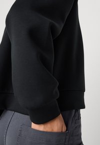 Felpa nera con una vestibilità rilassata, polsini a coste e una texture liscia, abbinata a pantaloni grigio scuro con tasche laterali.
