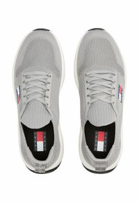 Sneakers grigi in maglia con una tomaia tessurizzata, lacci elastici e una suola intermedia bianca. Presentano una patch con il logo con accenti blu, rossi e bianchi.