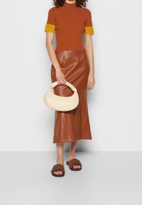 Ruskea raidoitettu neulepusero keltaisilla hihansuilla, ruskea nahkainen kellottava hame, kermahohtoinen käsilaukku ja ruskeat kuvioidut liukkaat sandaletit.