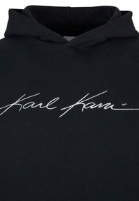 Sudadera negra con capucha ajustable. Presenta una firma bordada en blanco que dice "Karl Karin" en la parte frontal. Tejido de algodón suave.
