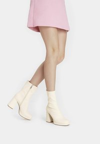 Botines de cuero blanco con tacón grueso y cremallera lateral, con una textura suave y diseño de punta redondeada.