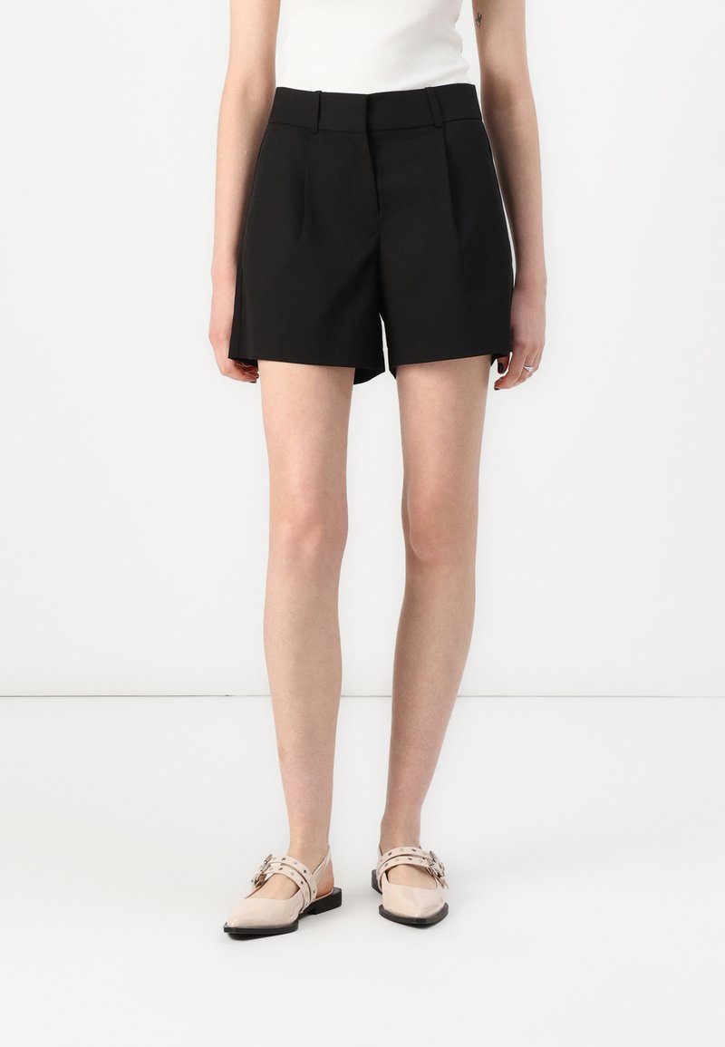 Shorts negri croiți, dintr-un material neted, cu talie înaltă, față pliată și buzunare laterale, asortați cu pantofi slip-on bej.