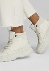 White high-top sneakers with smooth leather, rounded toe, and textured rubber sole. Features stitched accents and reinforced eyelets.