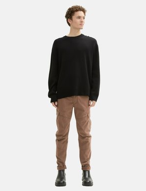 Schwarzer gerippter Pullover, beiges Cargo-Hose mit Klapptaschen und schwarze Stiefeletten. Einfaches Design, lässiger Schnitt, mit umgeschlagenen Säumen an der Hose.