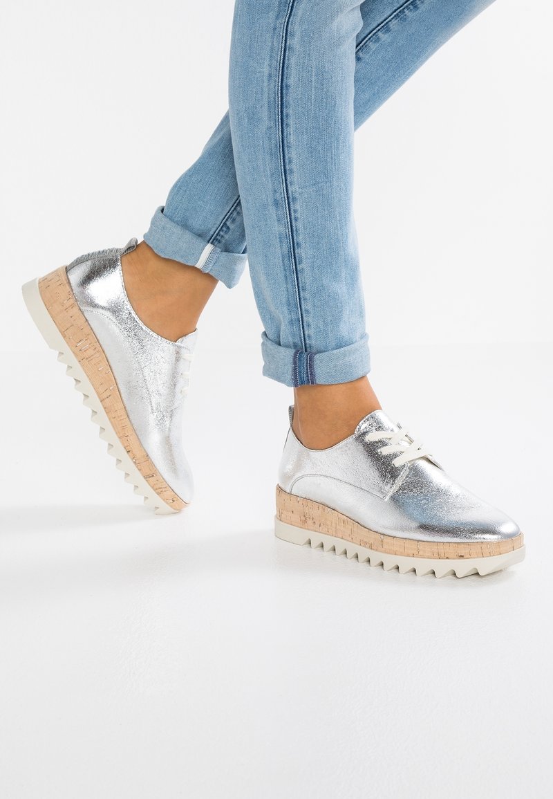 Chaussures métalliques argentées avec un design épuré, bout rond et semelle en liège texturée. Lacets blancs et semelle extérieure striée contrastante.