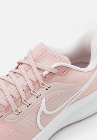 Helle rosa Sportschuh mit strukturiertem Obermaterial, weißen Schnürsenkeln und einem weißen Swoosh-Logo. Verfügt über eine gepolsterte Sohle und atmungsaktive Designelemente.