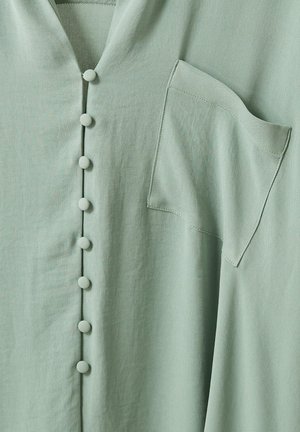 Hellgrünes Hemd aus Stoff mit stoffbezogenen Knöpfen vorne und einer einzigen Brusttasche auf der rechten Seite.
