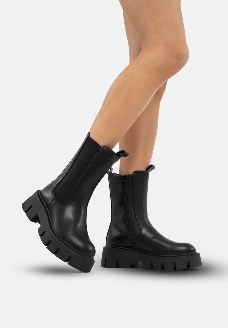Schwarze Lederstiefeletten mit einer klobigen Plattformsohle, elastischen Seitenpaneelen und Zuglaschen. Glatte Textur und runde Zehenform.