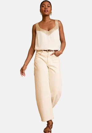 Beige sleeveless top with decorative gold accents, paired with high-waisted, wide-leg beige trousers. Notable belt detail and strappy sandals.