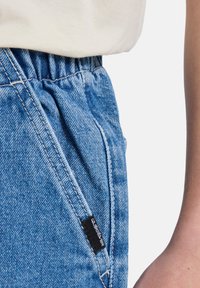 Light blue denim joggers with an elastic waistband, side pockets, and a black label detail near the pocket seam.