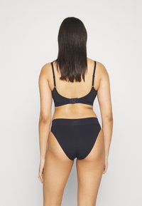 Set di reggiseno nero e perizoma coordinato; design senza cuciture con spalline regolabili e chiusura con gancio; tessuto morbido con una leggera lucentezza; branding minimale.