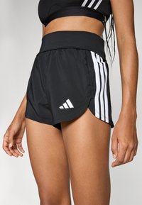Svart treningsshorts med bred livlinje, sidelommer og hvite akcentstriper med Adidas-logoen på nederkanten.