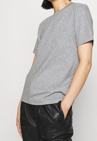 Grå bomulds t-shirt med korte ærmer og rund hals, vist sammen med sorte, strukturerede læderbukser. Enkel design uden mønstre.